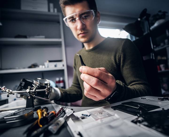 Electronic technician mending a broken phone, looking closely at the little bolt holding it with tweezers in the repair shop